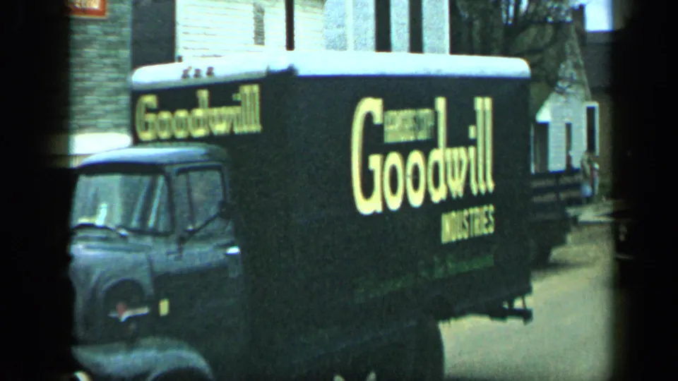 Close side view of the Goodwill Industries truck, with yellow branding visible against the dark body on a 1959 Aledo street.