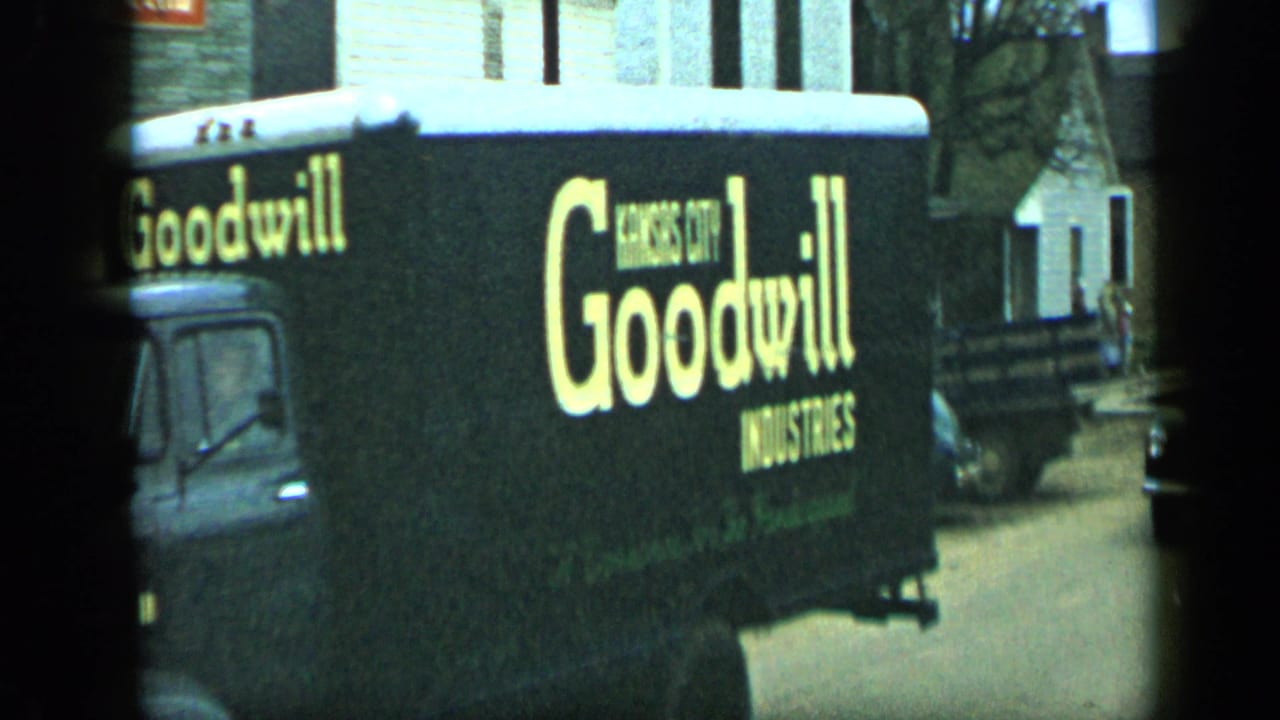 1959 Aledo, Texas 8mm frame showing a black Goodwill Industries truck with yellow lettering beside parked cars and houses.