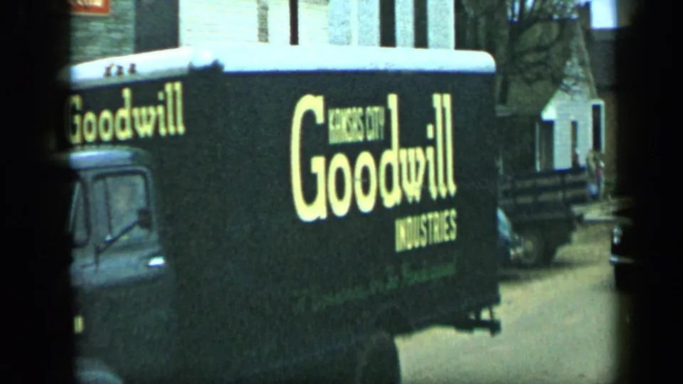 1959 Aledo, Texas 8mm frame showing a black Goodwill Industries truck with yellow lettering beside parked cars and houses.