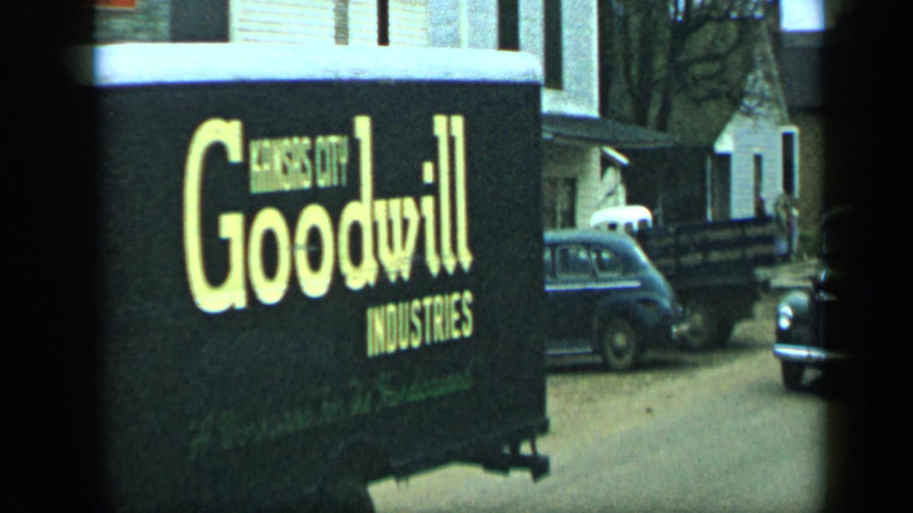 Side of a Goodwill Industries truck passing parked cars and houses.