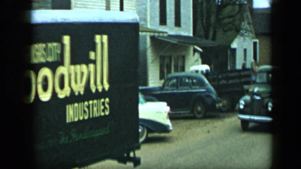 The truck moves out of frame, revealing parked mid-century cars and residential buildings in the 1959 Aledo, Texas clip.