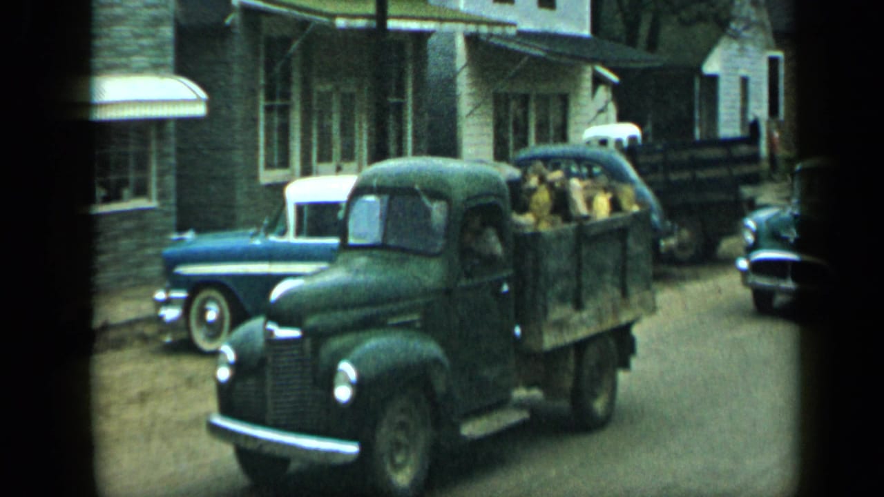 Dark green pickup truck passes parked cars on a residential street.