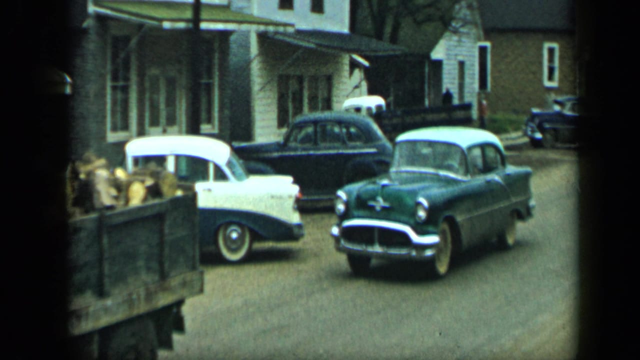 Vintage sedans parked on a residential street beside a produce-loaded truck.