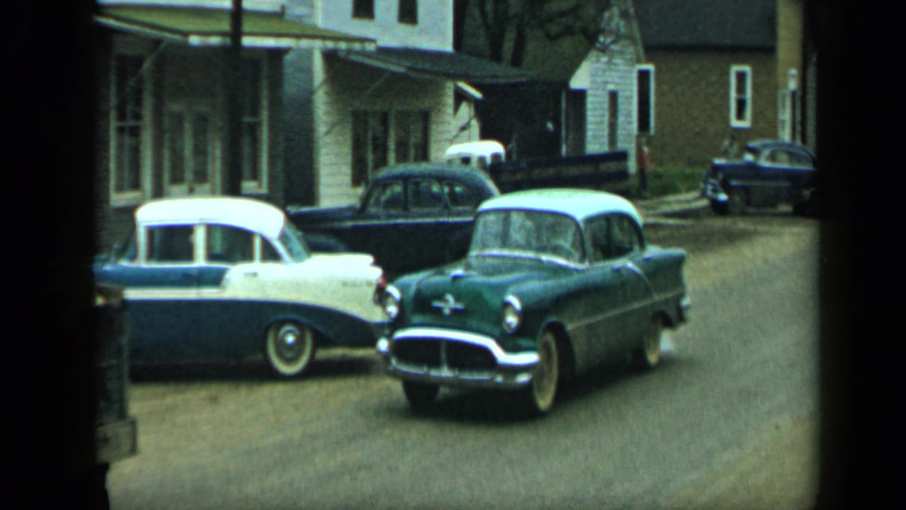 1959 Aledo, Texas street view with mid-century sedans parked or moving near frame houses and trees.