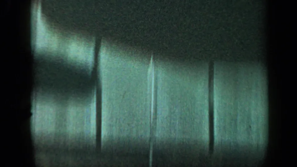 Partially obscured 8mm frame with dark film edge and a blurred exterior wall or siding surface, offering little subject detail.