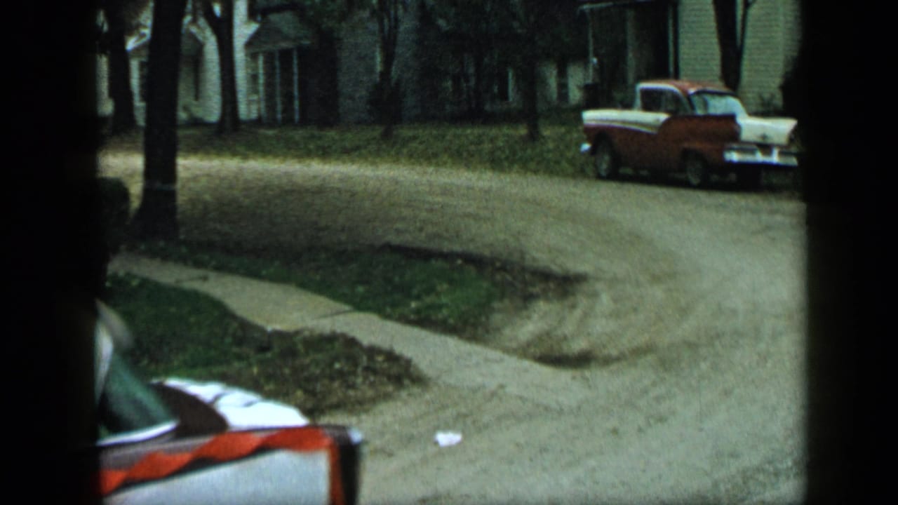 Red-and-white pickup parked on a curved residential road with houses and trees behind it.