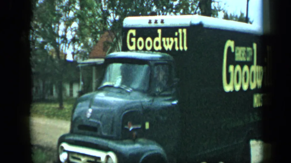 A black Goodwill Industries box truck with yellow lettering passes through a residential area in footage identified as Aledo, Texas in 1959.