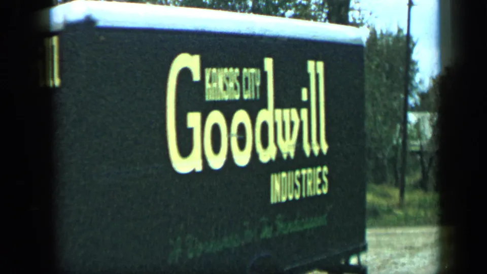 A close side view shows large yellow Goodwill Industries lettering on the moving truck, with trees and a residential roadside behind it.