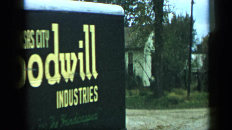 The Goodwill Industries truck continues past the camera, partly cropped by the film frame, with a quiet residential backdrop of trees and houses.
