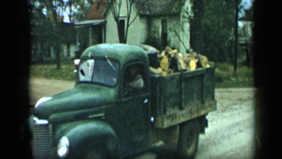 The firewood-loaded flatbed truck passes close to the camera on a residential street in 1959 Aledo, Texas.