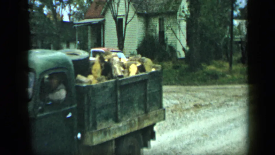 The loaded flatbed truck continues past modest houses in 1959 Aledo, Texas, with firewood visible in the bed.
