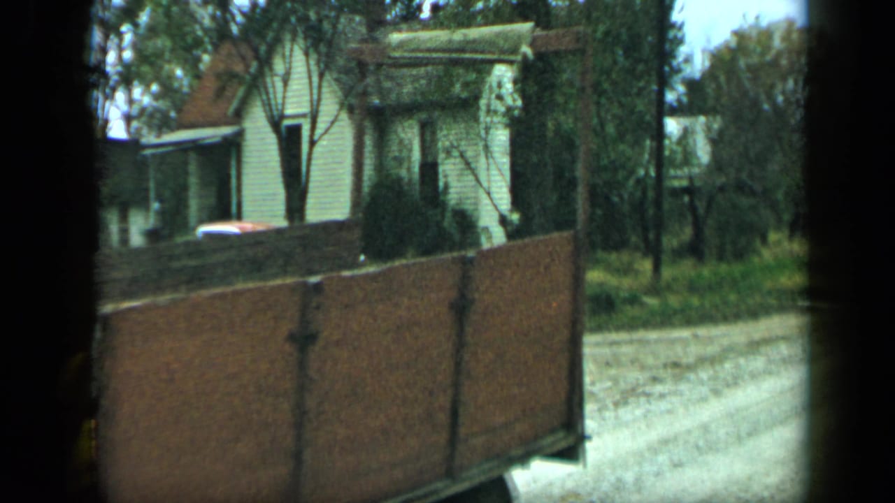Side of a wooden trailer on a quiet road with houses and trees in the background.