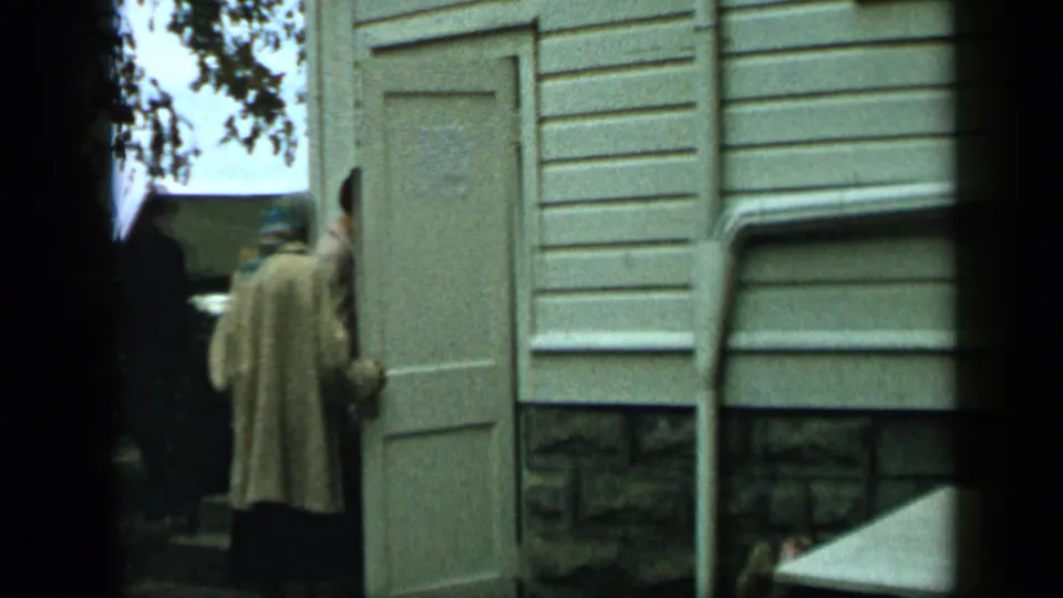 1959 Aledo, Texas home-movie frame showing the doorway open, with one adult entering and another partly obscured nearby.