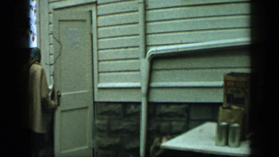 Aledo, Texas 1959 home-movie frame showing a person by a white door and a table with boxed groceries and metal cans.