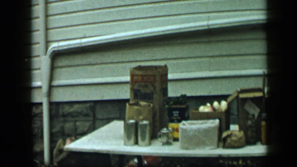 Aledo, Texas 1959 home-movie frame showing a table crowded with grocery boxes, cans, eggs, jars, and paper sacks.