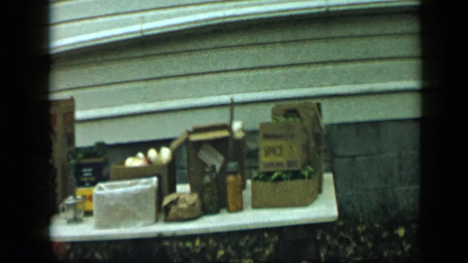 1959 Aledo, Texas home-movie frame showing household supplies on a white table, with branded packaging, produce, bags, and cans visible.