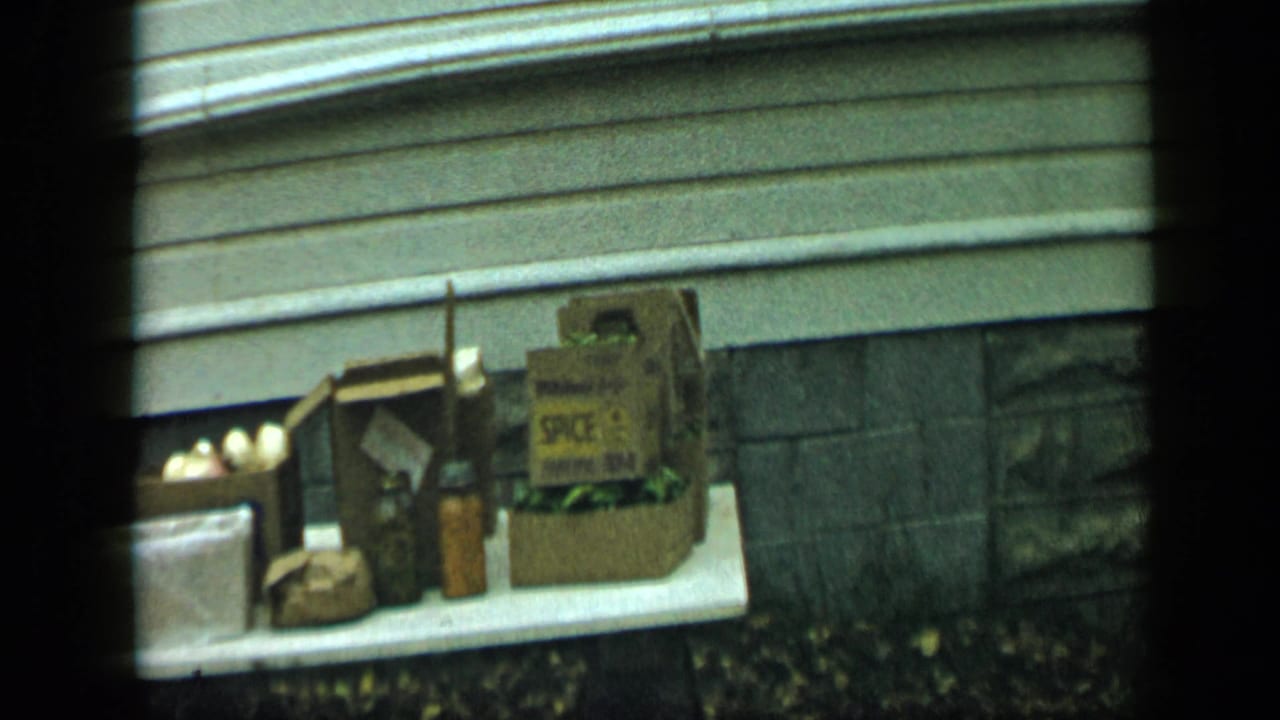 Cardboard boxes and jars sit on a white table against exterior siding and stonework.
