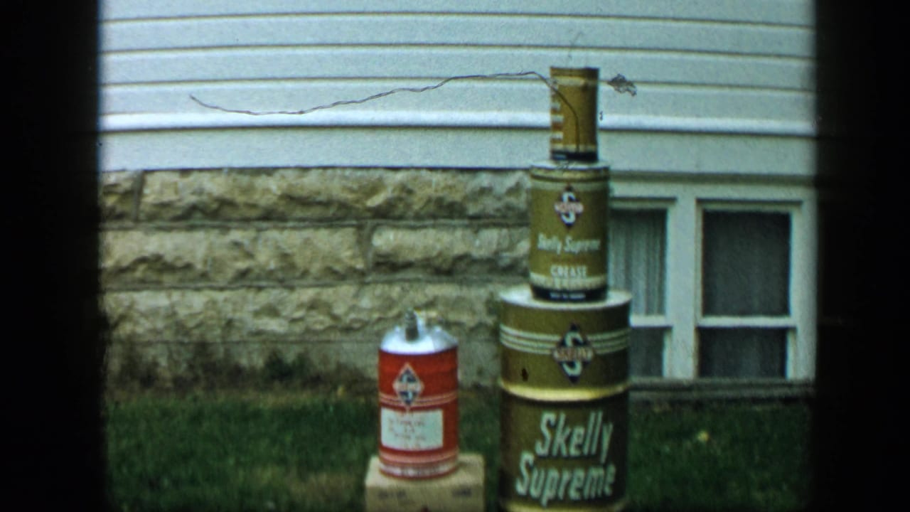 1959 Aledo, Texas frame with a red can near stacked Skelly Supreme containers outside a residential wall.