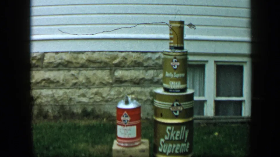1959 Aledo, Texas frame with a red can near stacked Skelly Supreme containers outside a residential wall.