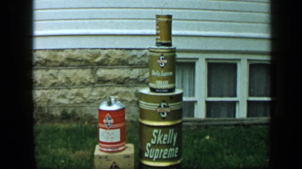 1959 Aledo, Texas frame focused on a stack of Skelly Supreme containers and a red can in a residential yard.