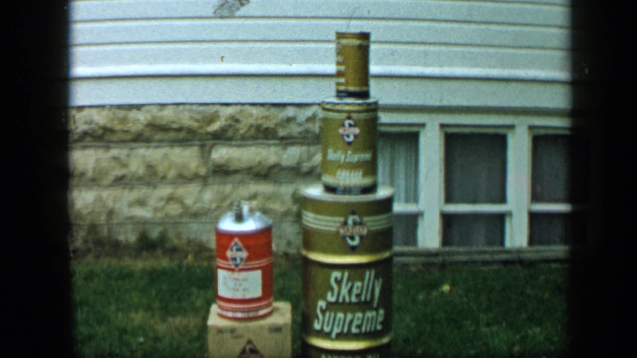 Stacked Skelly Supreme cans outside a house with basement windows and grass.