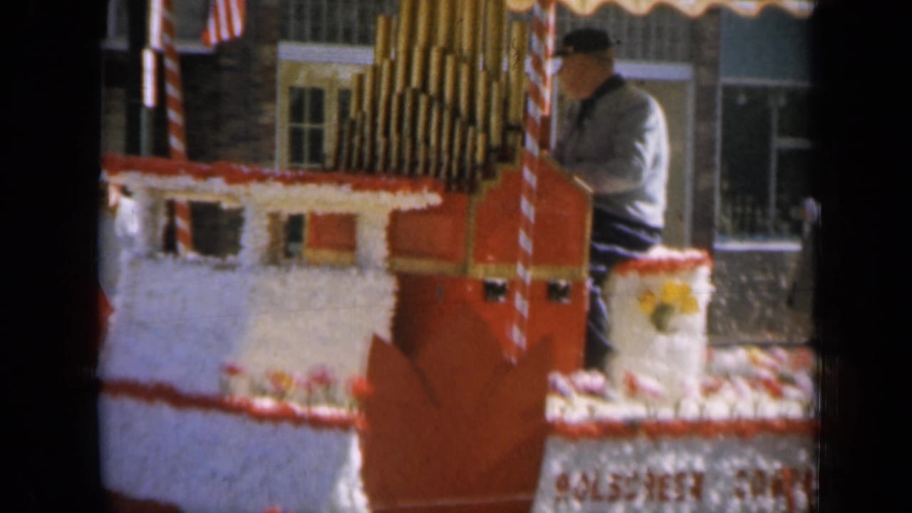 Man at a decorated parade float with calliope pipes and American flags.