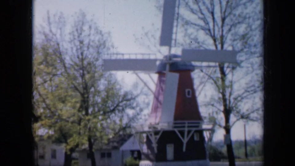 The windmill appears from a slightly shifted home-movie angle, with trees, grass, and small buildings around it.