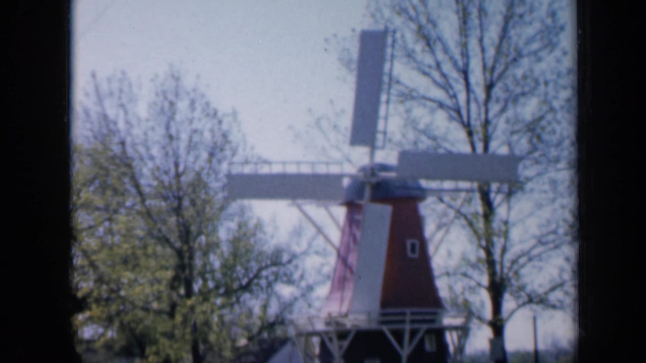 Red-and-white windmill standing among trees in daylight.