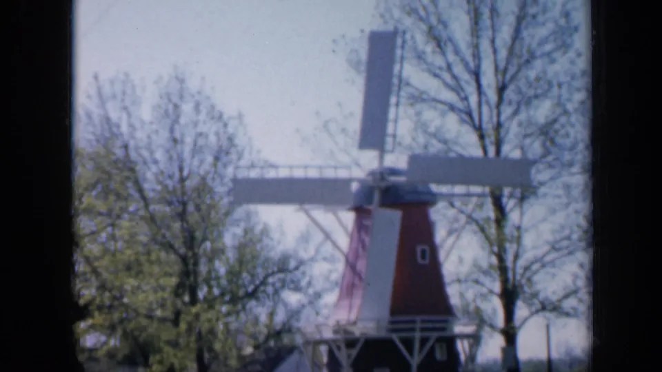 1959 Iowa 8mm frame showing a red-and-white windmill near trees under bright daylight.