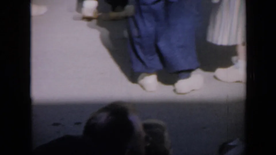1959 Iowa 8mm frame showing dancers' lower bodies, white shoes, blue pants, and a striped skirt with a partial head at the bottom edge.