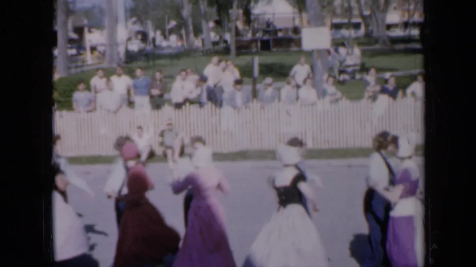 Costumed dancers in pink, purple, and pale dresses move in formation during an Iowa public performance in 1959.