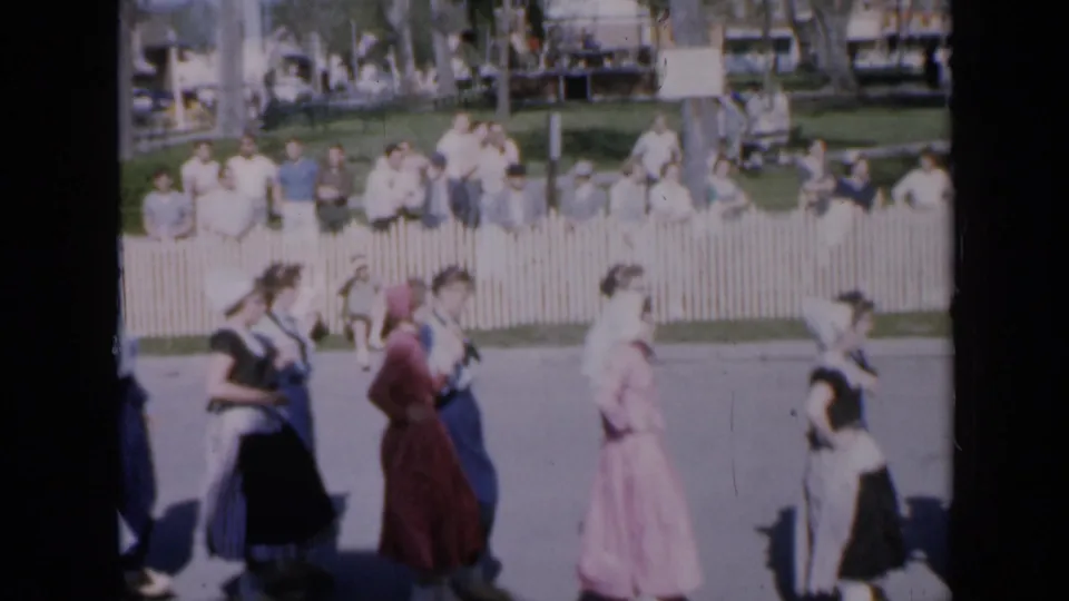 Several dancers in long skirts and fitted bodices cross the paved performance area while spectators watch in the background.