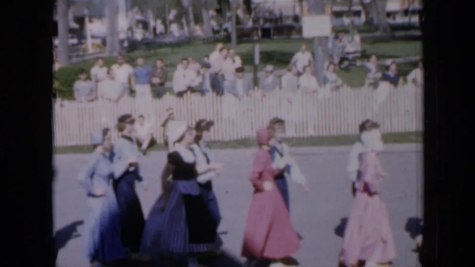 Dancers in blue, pink, and pale dresses pass the camera during the 1959 Iowa community performance.