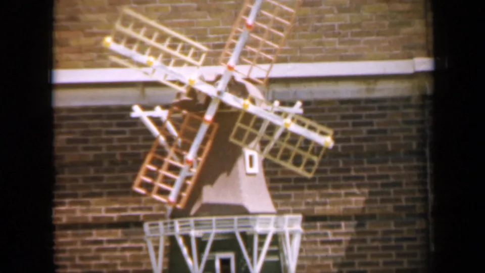 1959 Iowa 8mm still with the decorative windmill filling the frame, its blades crossing the brick background.