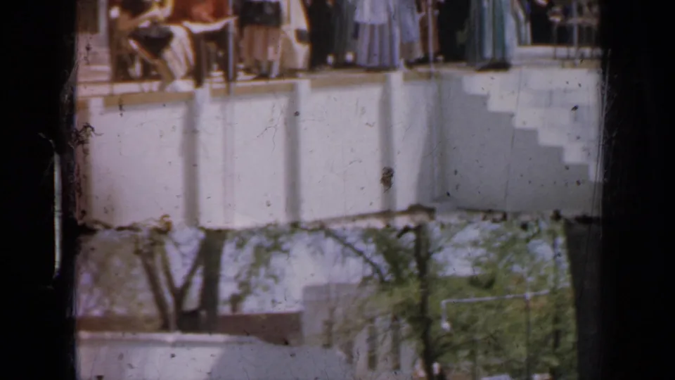 Late-1950s Iowa home-movie frame of formal guests gathered on an outdoor balcony or terrace.