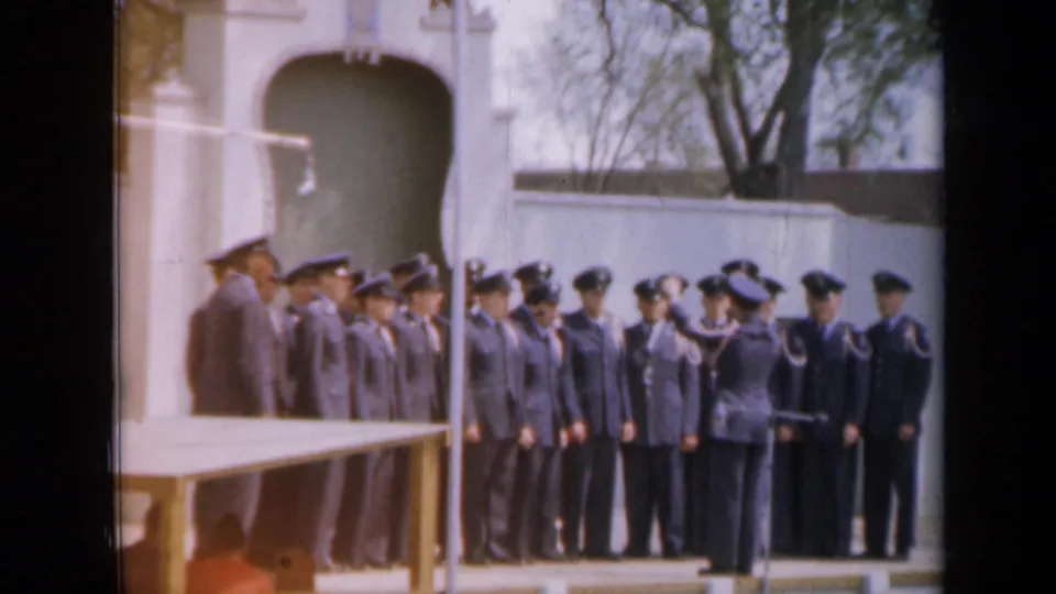 In Iowa, 1959 per metadata, an officer salutes or addresses uniformed personnel in formation before a white arched structure.