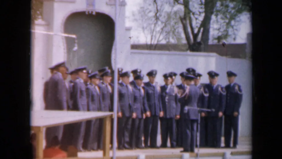 The 1959 Iowa footage shows uniformed personnel lined up in front of a white arched monument while an officer addresses them.