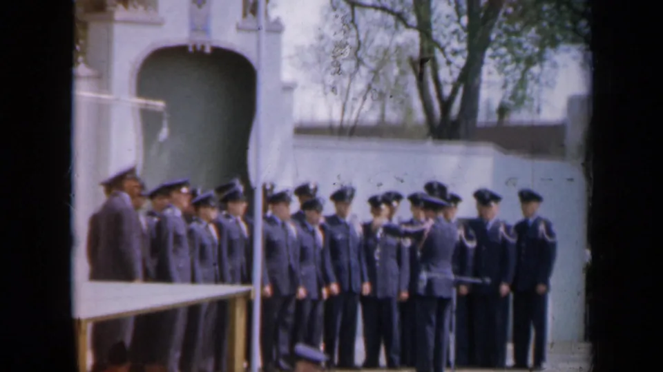 In the final frame, an officer gestures toward the uniformed formation during the outdoor Iowa ceremony documented as 1959.