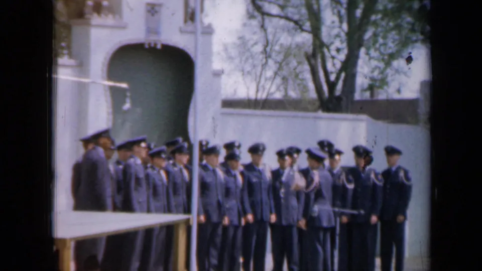 A 1959 Iowa home-movie frame shows cadets in dark caps and uniforms standing in formation during outdoor instruction.