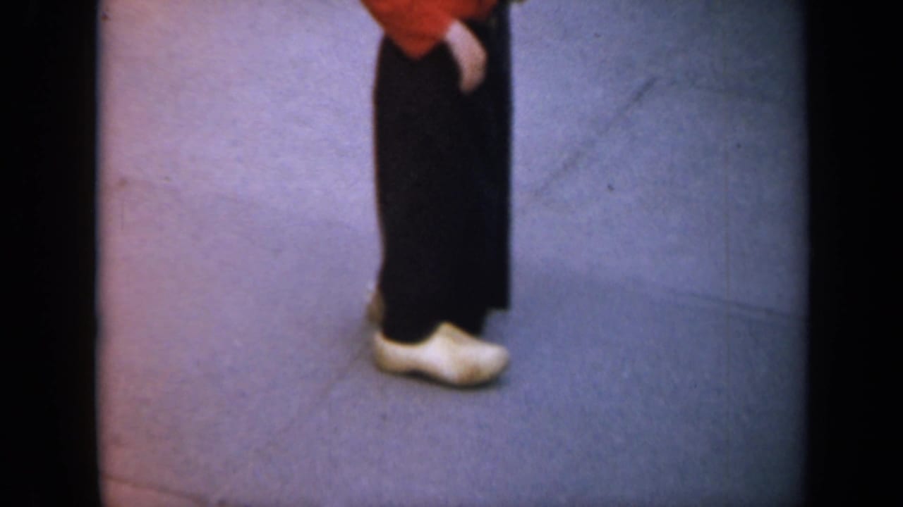 Close view of a person in dark clothing and white wooden clogs walking past the camera.