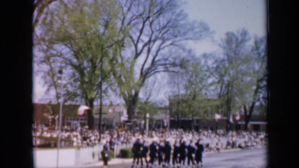 1959 Iowa street parade view with a uniformed group in formation and a large crowd watching from the far side.