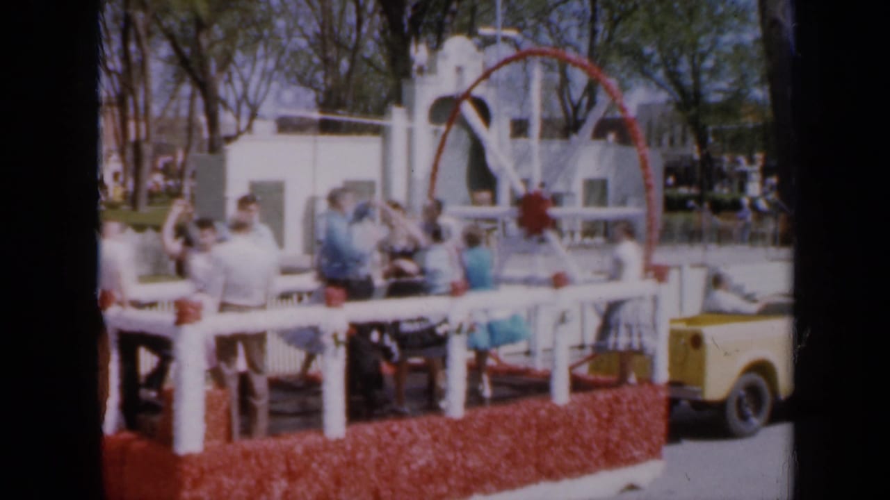 Decorated parade float with people standing near a large red-and-white wheel.