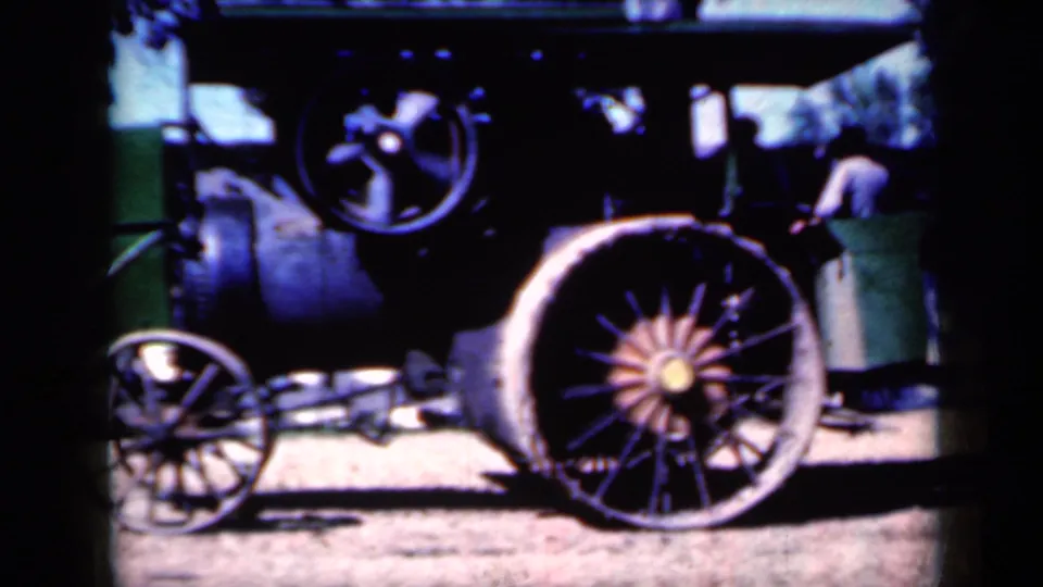A steam tractor with large spoked wheels is shown in Iowa home-movie footage, with a partly visible person standing near the machinery.