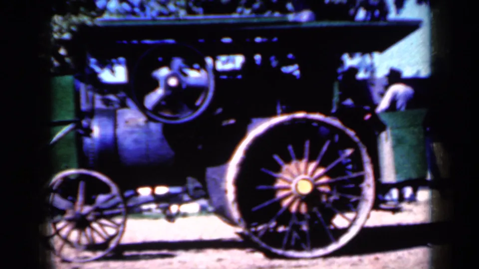 The side of a steam tractor fills the frame, showing spoked wheels, mechanical parts, and a partly visible person near the right edge.
