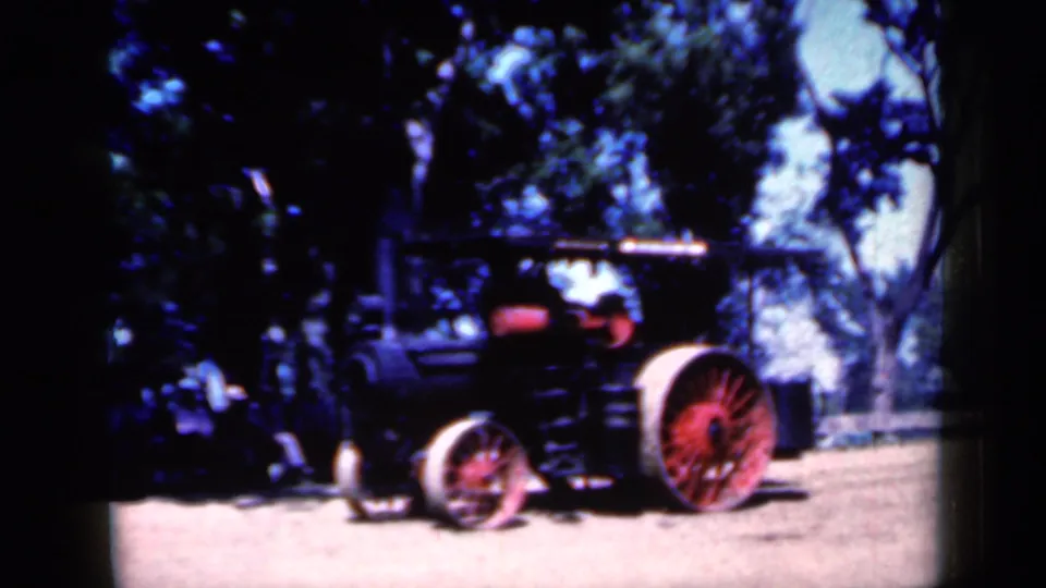 Final frame of the 1959 Iowa clip shows the steam-powered tractor moving past trees, with the red rear wheel and smokestack visible.