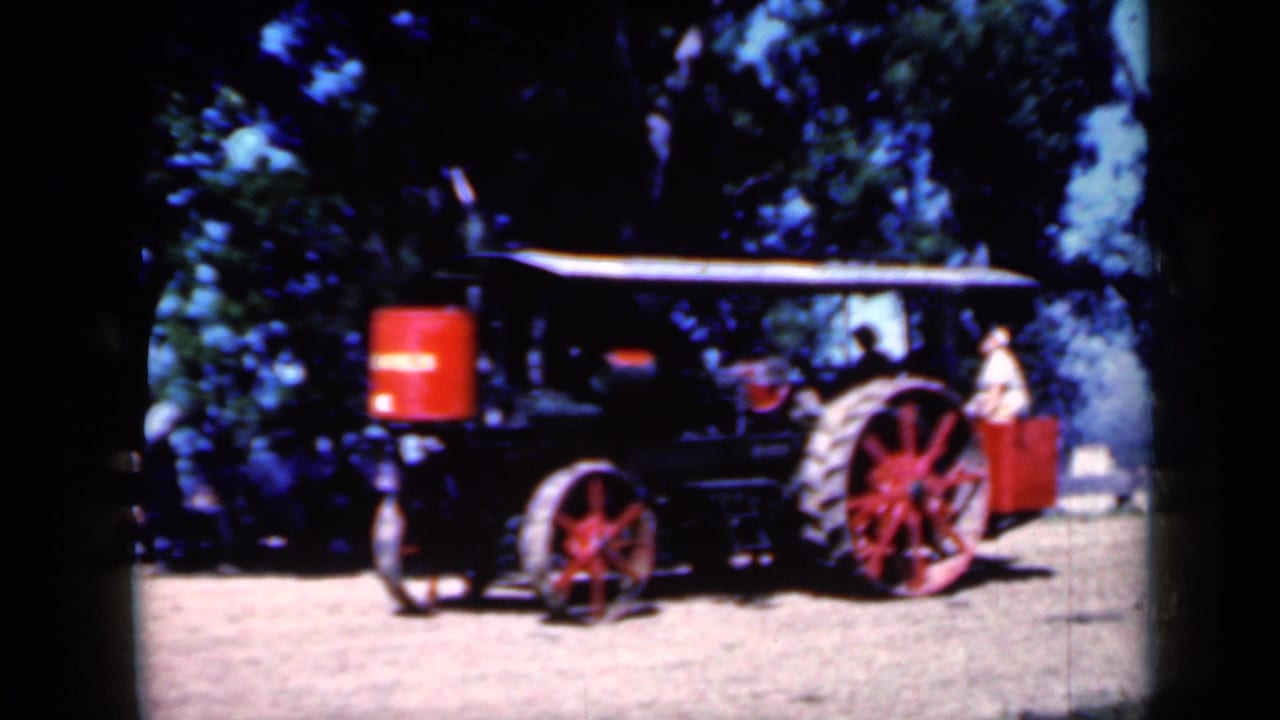 Side view of the black and red steam traction engine in Iowa, with a light-clothed person visible near the rear of the machine.