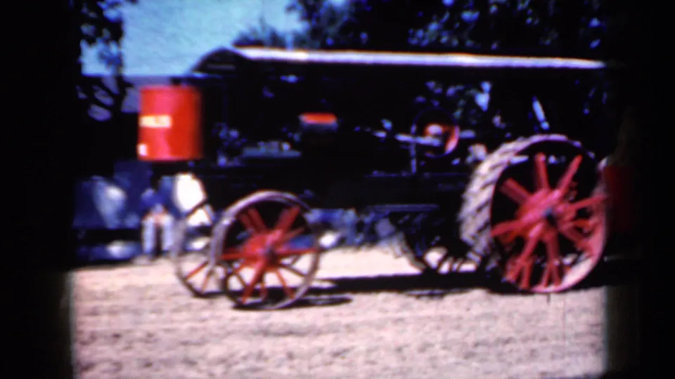Close side view of the vintage steam traction engine in Iowa, with red spoked wheels, black machinery, canopy roof, and dirt foreground.