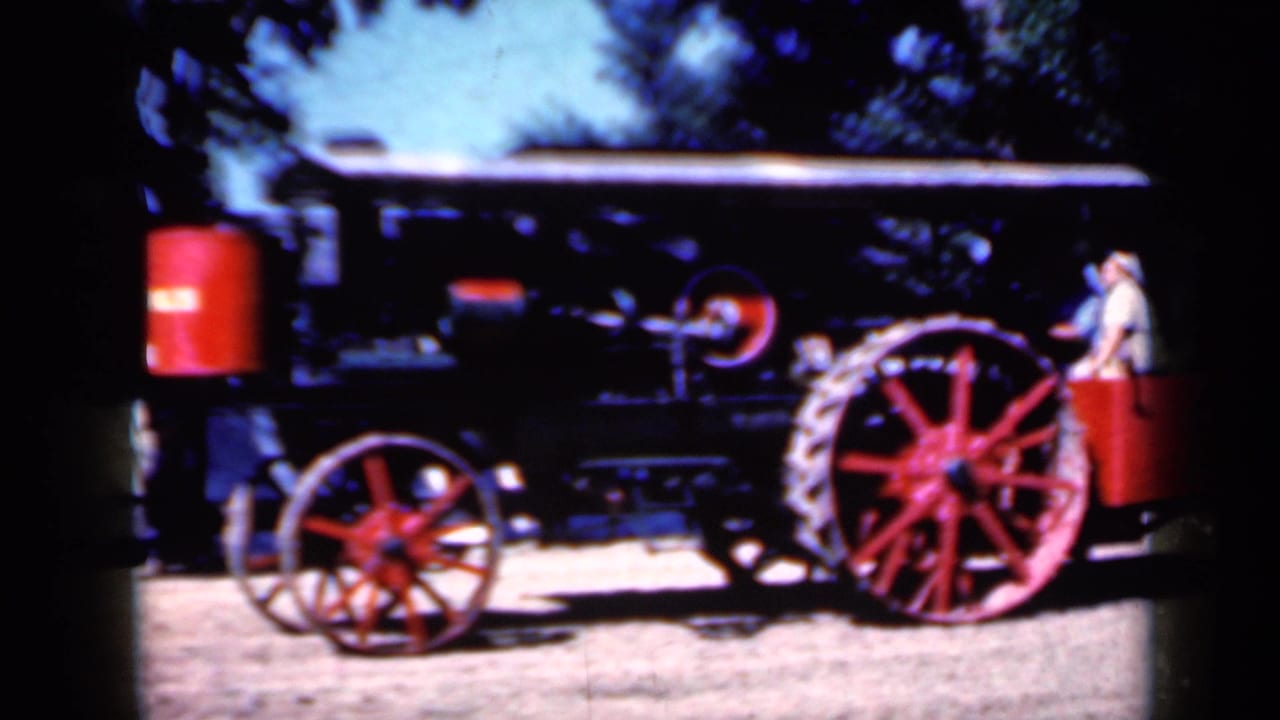 1959 Iowa home-movie frame of a black steam tractor with red wheels, canopy, and a light-clothed person beside the rear section.