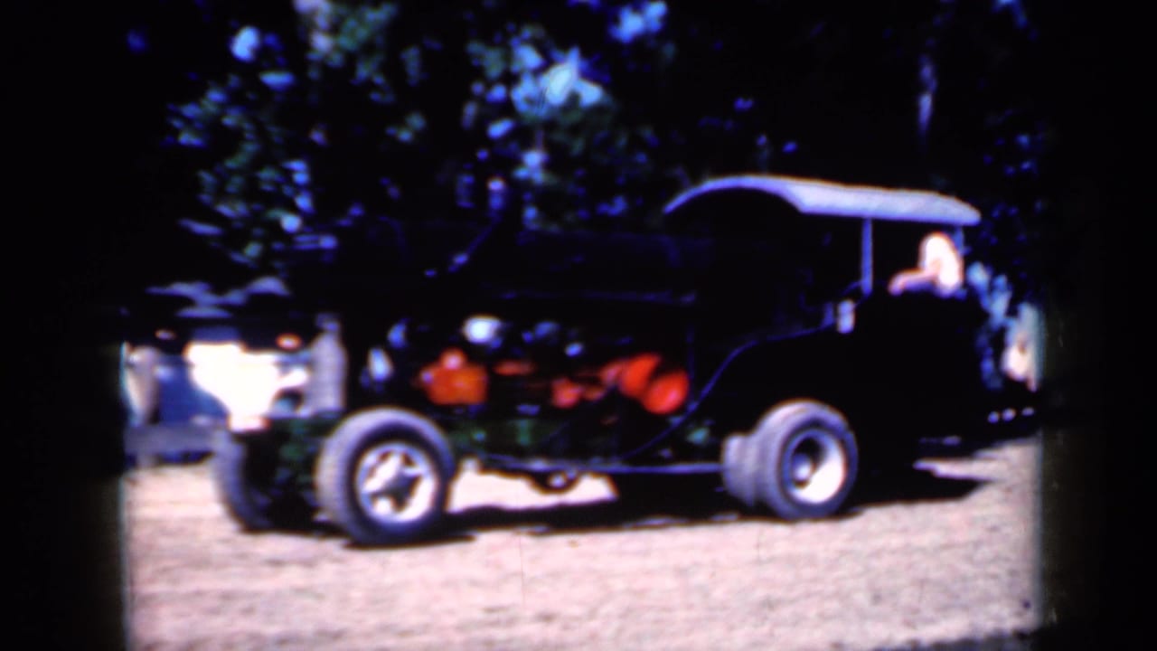 Black vintage steam tractor with white canopy on a dirt field near trees.