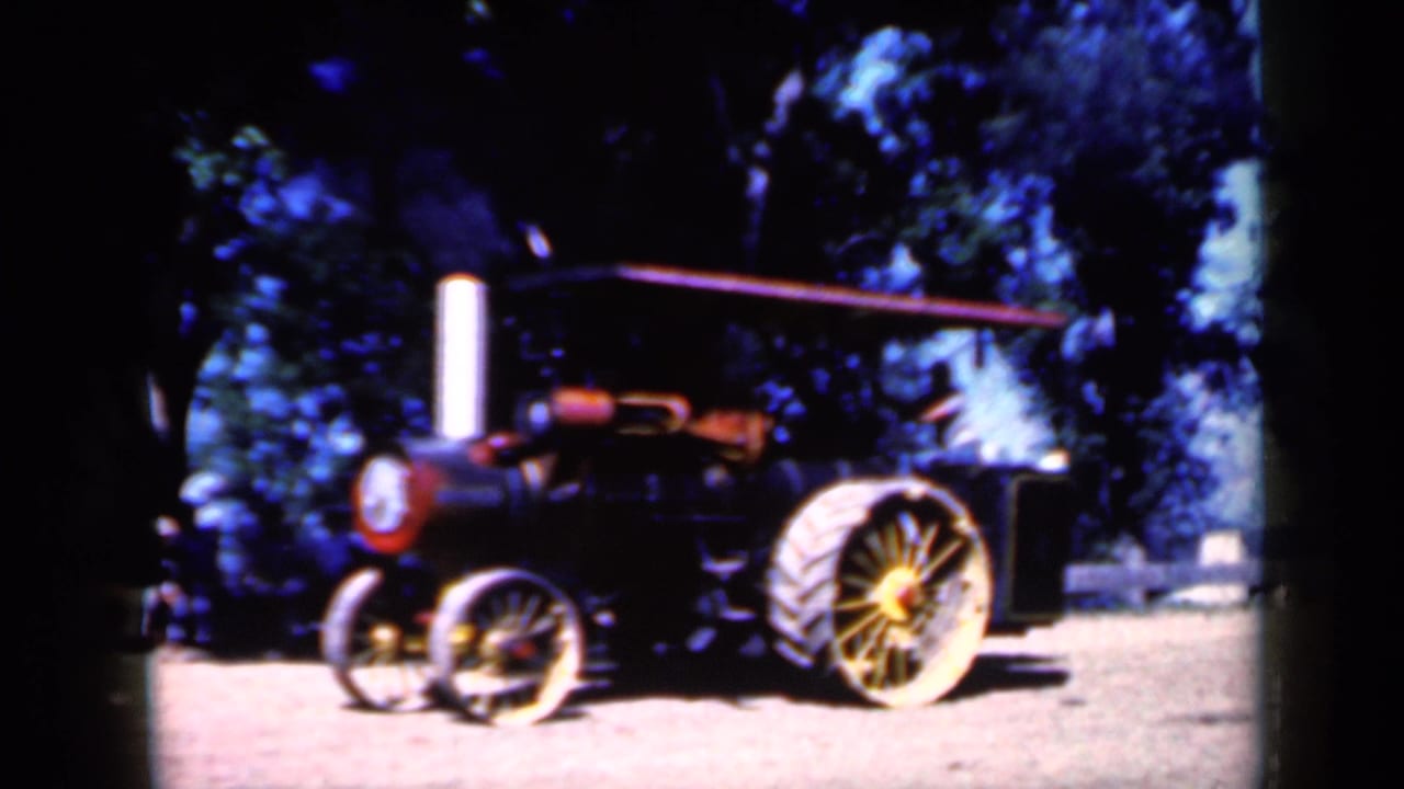 Red and black steam traction engine parked on dirt under trees.